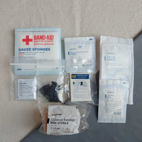 First aid kit pouch containing gauze pads latex gloves compressed gauze bzk wipes eye pad and cohesive bandage in baggies