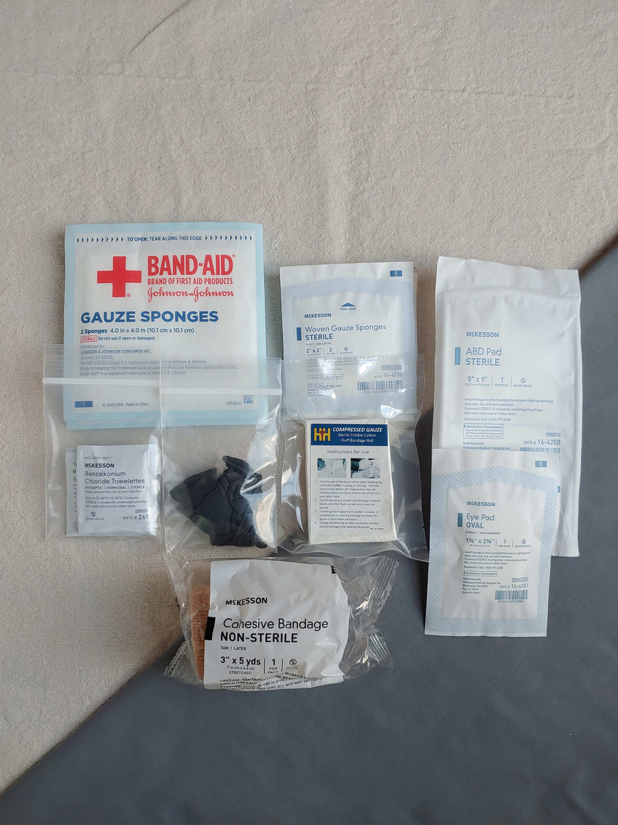 First aid kit pouch containing gauze pads latex gloves compressed gauze bzk wipes eye pad and cohesive bandage in baggies
